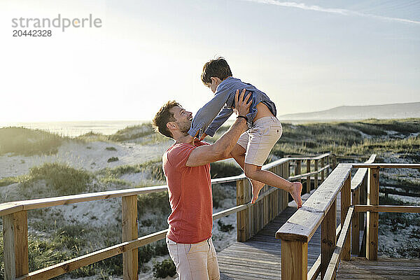 Father carrying son from boardwalk railing at beach