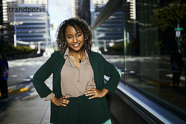 Smiling beautiful young businesswoman standing with arms akimbo