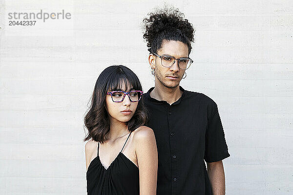 Young man and woman wearing eyeglasses in front of white wall