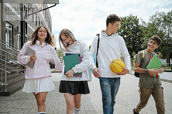 Happy teenage boys and girls walking together at schoolyard