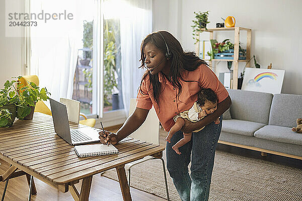 Freelancer writing in diary and standing with daughter at home