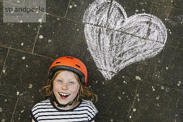 Happy girl lying down near heart shape drawing on ground