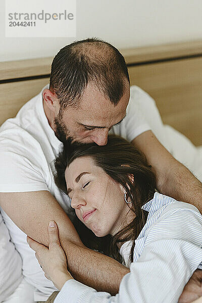 Man kissing woman lying on bed at home