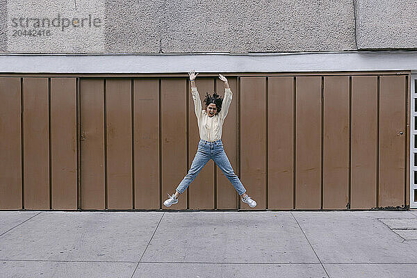 Cheerful woman jumping in front of brown wall