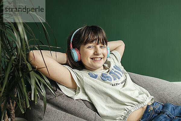 Happy girl listening to music over headphones sitting on pouffe