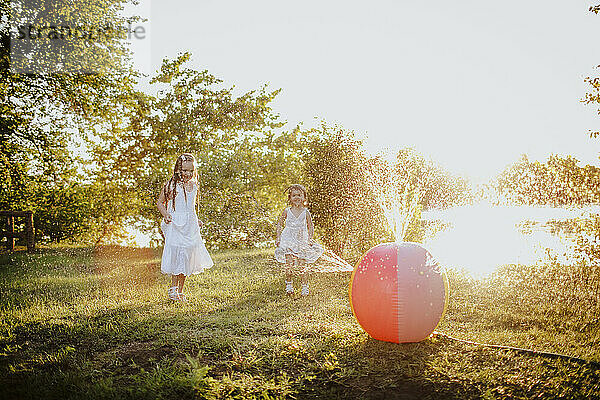 Siblings playing near colorful ball splashing water at garden