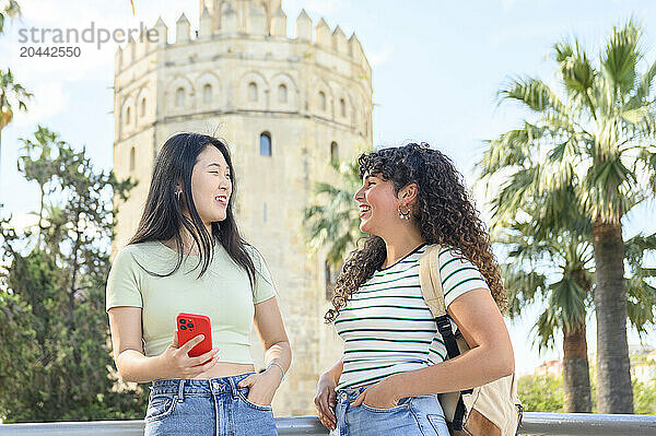 Happy friends sharing smartphone in front of Torre del Oro