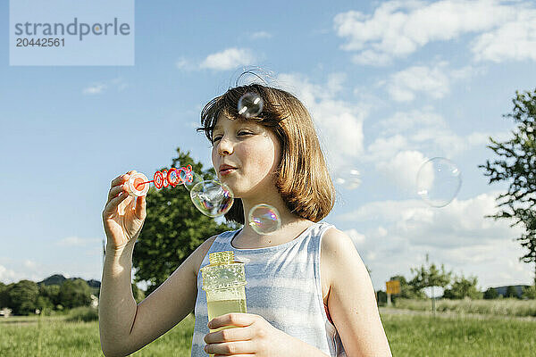 Happy girl blowing soap bubbles in field on sunny day