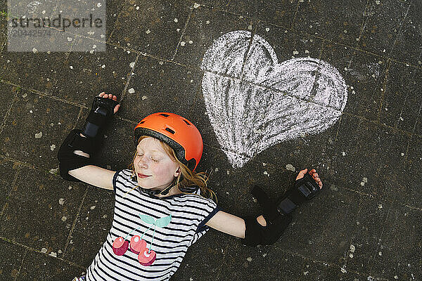 Girl lying down with eyes closed near heart shape drawing on ground