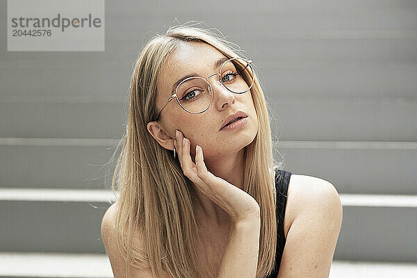 Young woman with blond hair wearing eyeglasses sitting on steps