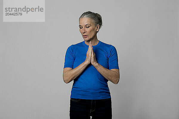 Senior woman with hands clasped in front of wall