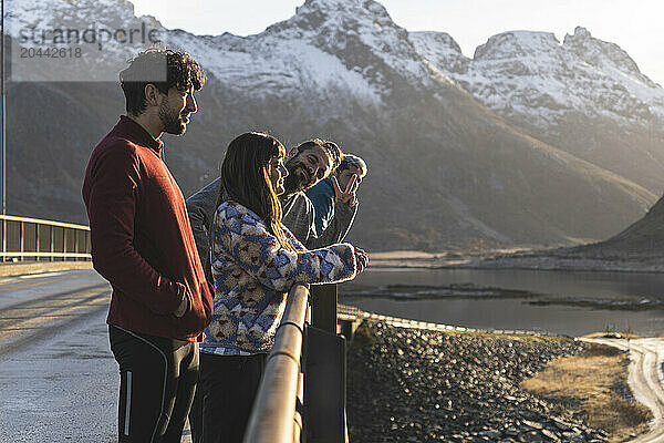 Norway  Nordland County  Group of young people standing on coastal bridge in Lofoten islands at dusk