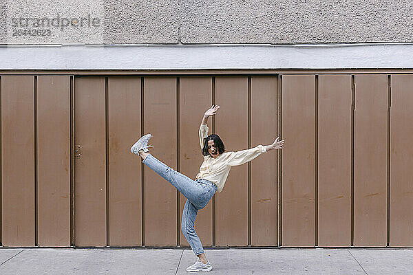 Happy woman dancing and having fun in front of brown wall