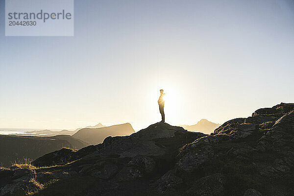 Man standing on top of rock at mountain peak in Norway