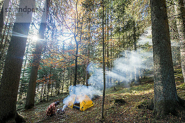 Senior man preparing food near tent in forest