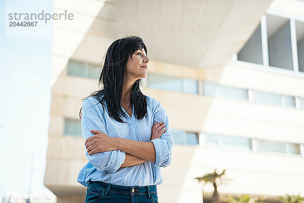 Thoughtful businesswoman with arms crossed in front of building