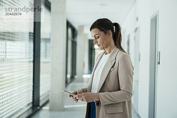 Businesswoman using smart phone near corridor of office