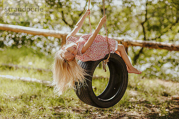 Blond girl bending backwards swinging on tire at garden