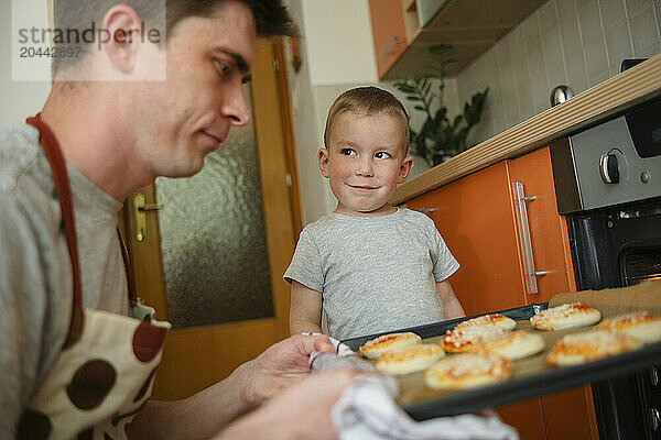 Cute boy Standing near father in kitchen at home