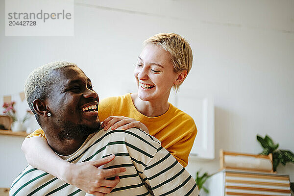 Smiling young woman with arm around looking at boyfriend in kitchen