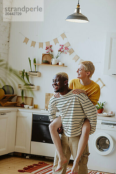 Happy man piggybacking girlfriend in kitchen