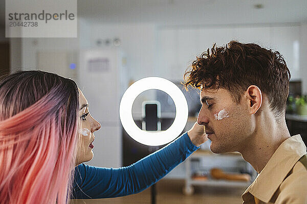 Influencer applying face cream on friend and vlogging at home