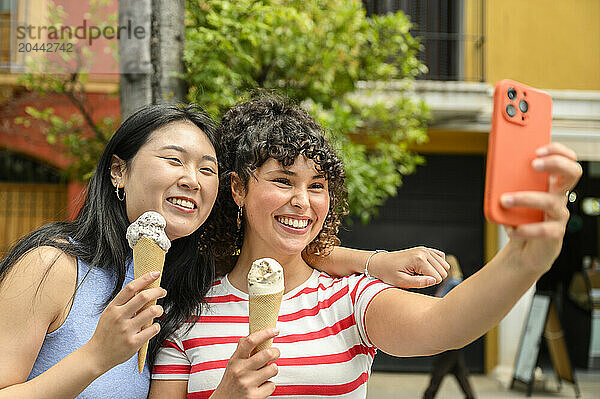 Smiling friend eating ice cream and taking selfie at street