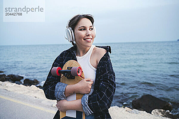 Woman embracing skateboard listening to music at beach