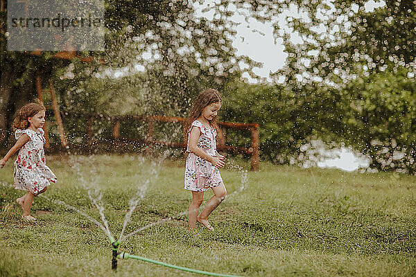 Girls running near garden hose splashing water on grass