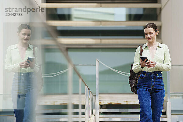 Woman walking and using smartphone near building