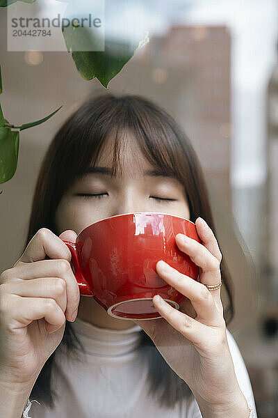 Young woman drinking coffee in cafe seen through glass