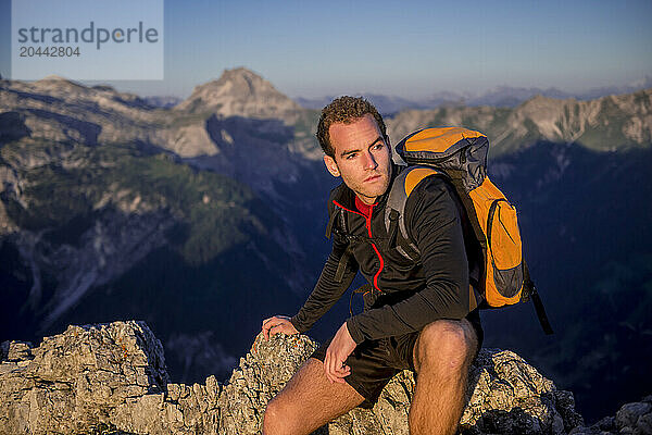 Young man sitting on Steinfeldspitze rock under sky at sunrise in Altenmarkt  Zauchensee  Salzburg  Austria