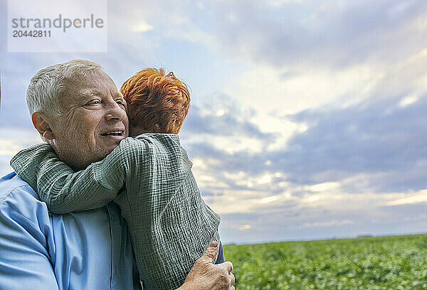 Redhead boy hugging grandfather at field