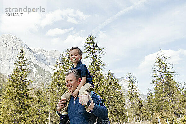 Happy father carrying son on shoulders near trees