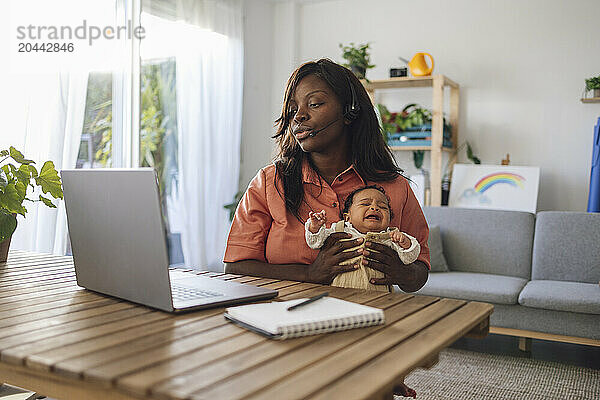 Busy freelancer working and holding crying daughter at home