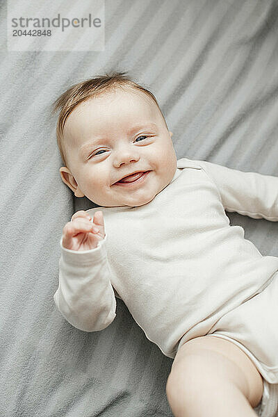 Smiling baby boy lying on gray blanket