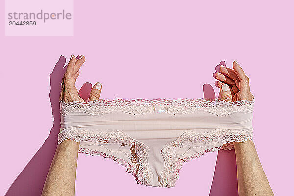 Hands of woman stretching underwear over pink background