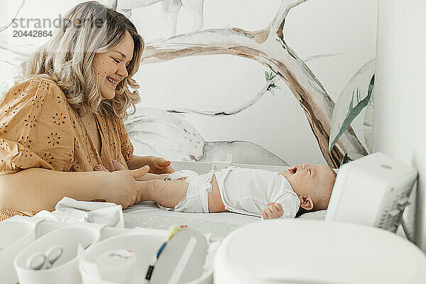 Mother changing clothes of baby boy on table