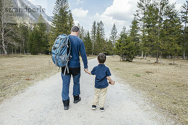 Father and son walking on road in front of trees