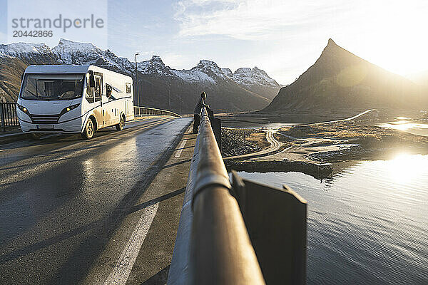 Norway Â NordlandÂ County  Young man standing on coastal bridge inÂ LofotenÂ islands at sunset