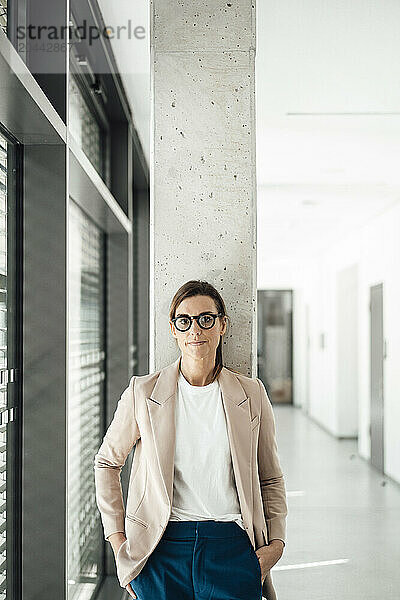 Businesswoman wearing eyeglasses with hands in pocket standing at office