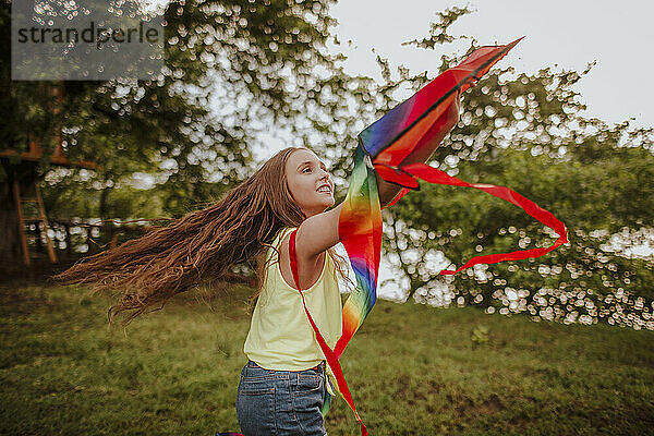 Smiling redhead girl flying kite in garden at sunset