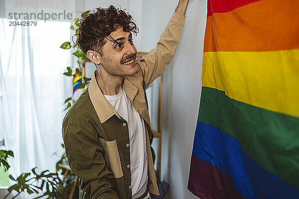 Happy non-binary person hanging rainbow flag on wall