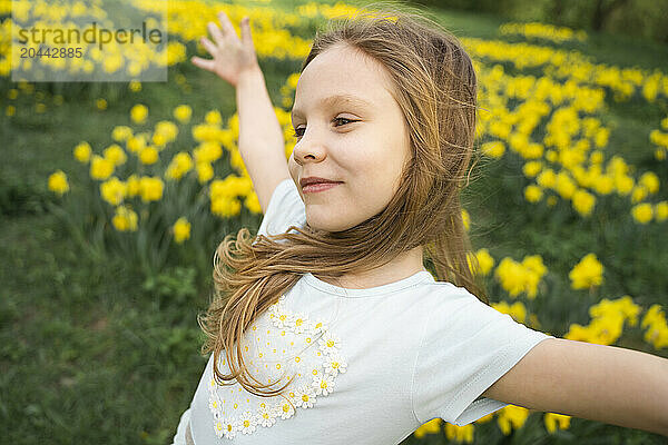 Smiling cute girl standing with arms outstretched in daffodil field