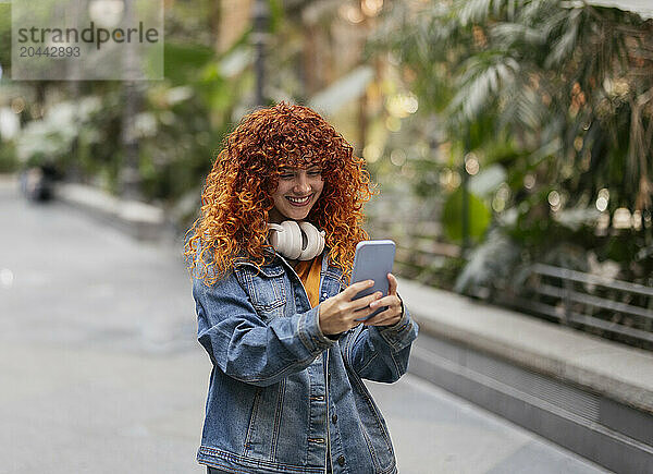 Happy young redhead woman with curly hair using smart phone