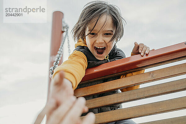 Playful boy reaching for fathers hand at park