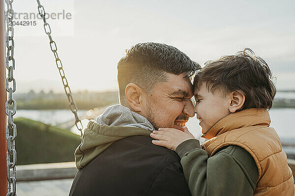 Happy son and father rubbing noses at park