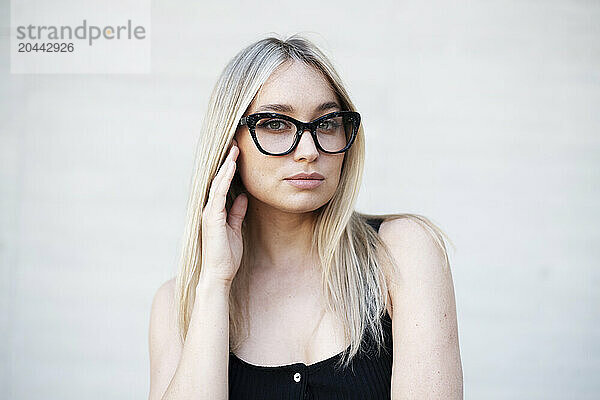 Confident blond young woman wearing eyeglasses in front of white wall