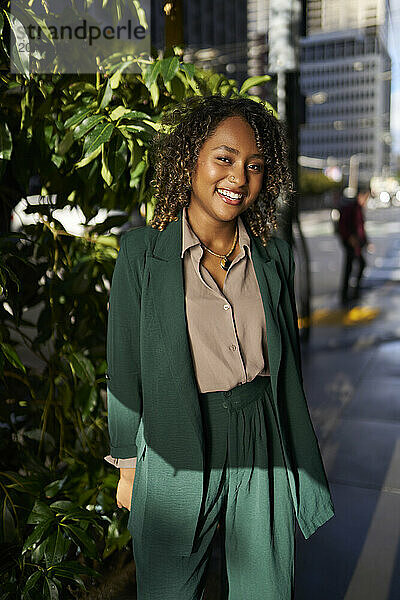 Happy beautiful young businesswoman standing in front of plant