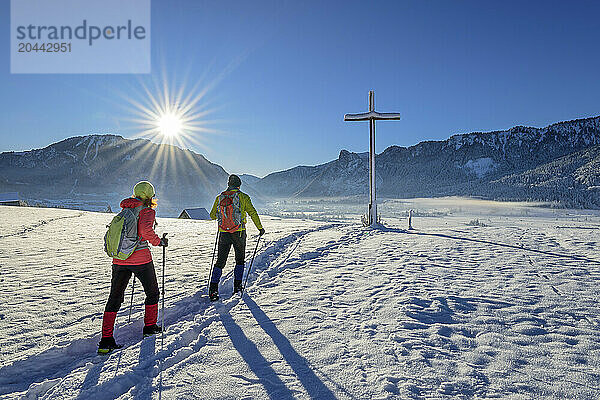 Man and woman hiking towards summit cross in winter  Altherrensteig  Ammergau Alps  Upper Bavaria  Bavaria  Germany